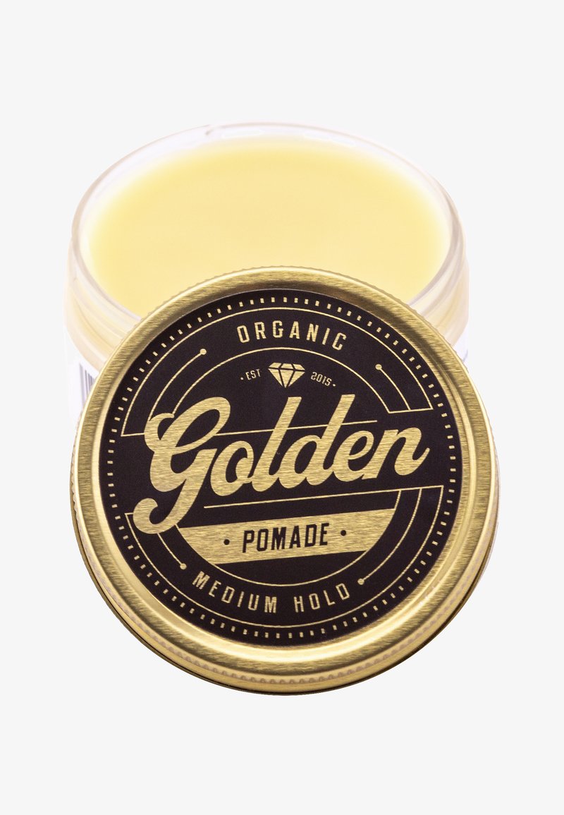Gyllene och svarta plåtburk med ekologisk pomada med ett runt lock; texten lyder "Golden Pomade" och "Medium Hold", med en glänsande yta.