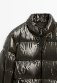 Daunenjacke in Dunkelgrün mit hohem Kragen, glänzender Steppstruktur und einem Reißverschluss vorne. Weiches, leichtes Material.