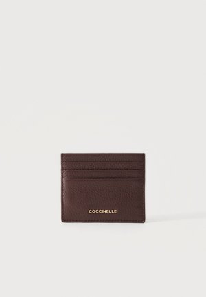 Porte-cartes en cuir brun texturé avec quatre emplacements pour cartes et logo doré "COCCINELLE" centré sur le devant.