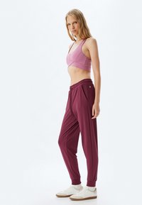 Sportbeha in lichtroze met een kruisrugontwerp; paarse joggingsbroek met zijzakken, elastische taille en taps toelopende boorden; witte sneakers.