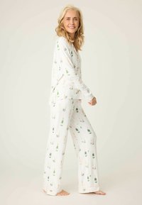 Vitt pyjamas-set med ett blom- och champagneflaskmönster; långärmad topp med rundad nederkant, mjukt tyg och löst sittande byxor.