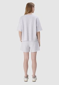 Jasnoszara, oversize t-shirt z krótkimi rękawami, połączona z dopasowanymi szortami. Casualowy design z postrzępionymi brzegami. Noszone z białymi sneakerami.