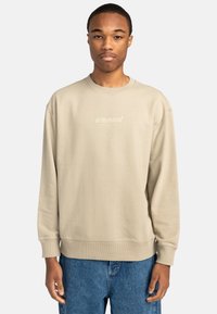 Beige bomulls sweatshirt med rund halsringning, lös passform och ribbade ärmmuddar. Har en subtilt tryckt "element"-logotyp. Bärs tillsammans med blå jeans.