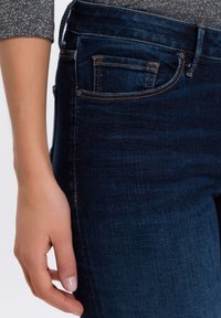 Donkerblauwe jeans hebben een klassieke vijf-pocketontwerp, met contrasterende oranje stiksels, een gladde textuur en een slanke pasvorm.