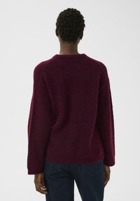 Pull en tricot bordeaux avec une texture douce, coupe ample et manches raglan. Ourlet et poignets côtelés. Vue arrière avec un design simple, sans motifs.