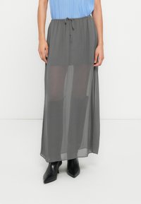 Μακριά, ελαφριά, διαφανής γκρι φούστα με κορδόνι στη μέση, υφή υφάσματος, συνδυασμένη με μαύρα μυτερά μποτάκια αστραγάλου.