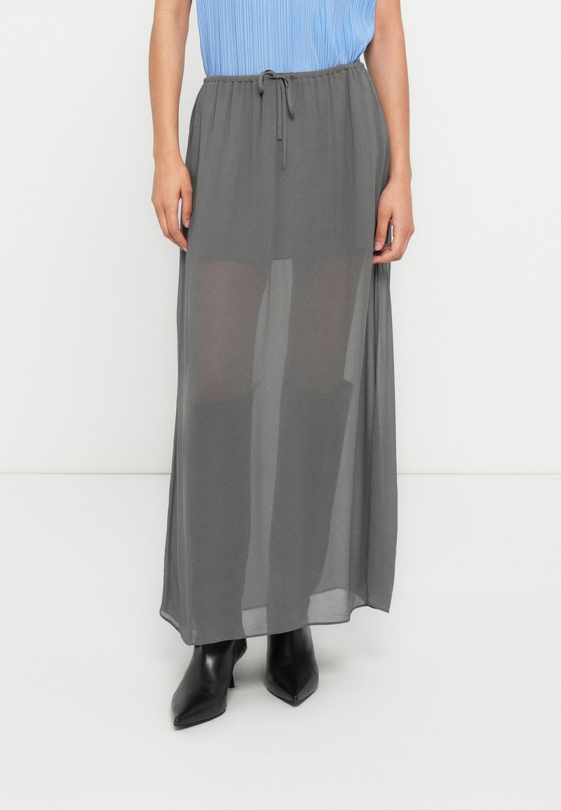 Μακριά, ελαφριά, διαφανής γκρι φούστα με κορδόνι στη μέση, υφή υφάσματος, συνδυασμένη με μαύρα μυτερά μποτάκια αστραγάλου.