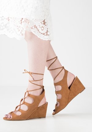 Sandales compensées en suède marron avec lacets à la cheville, bout ouvert et design découpé sur l'empeigne. Surface texturée et talon profilé.