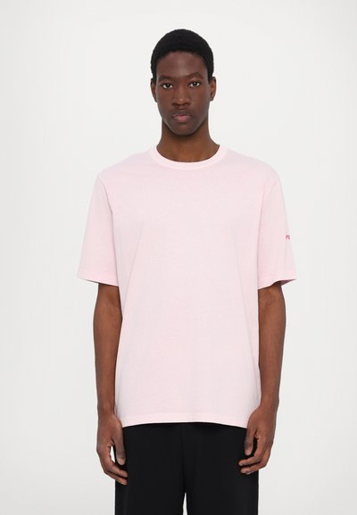Helles rosa Baumwoll-T-Shirt mit rundem Halsausschnitt und kurzen Ärmeln, mit einem kleinen Logo auf dem linken Ärmel, an einem Modell präsentiert.