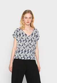 Top floral de manga curta em branco com flores azul-marinho, apresentando um design de decote em V e um caimento fluido. Tecido suave com textura subtil.