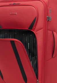 Rode koffer met een gestructureerde nylon buitenkant, voorzien van zwarte accenten, meerdere ritsen en een gestreepte binnenvoering met branding.