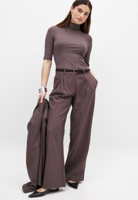 Högmidjade, vida byxor i dämpad lila tyg, kombinerade med en ribbad turtleneck och ett bälte. Svarta spetståskor och en blazer.
