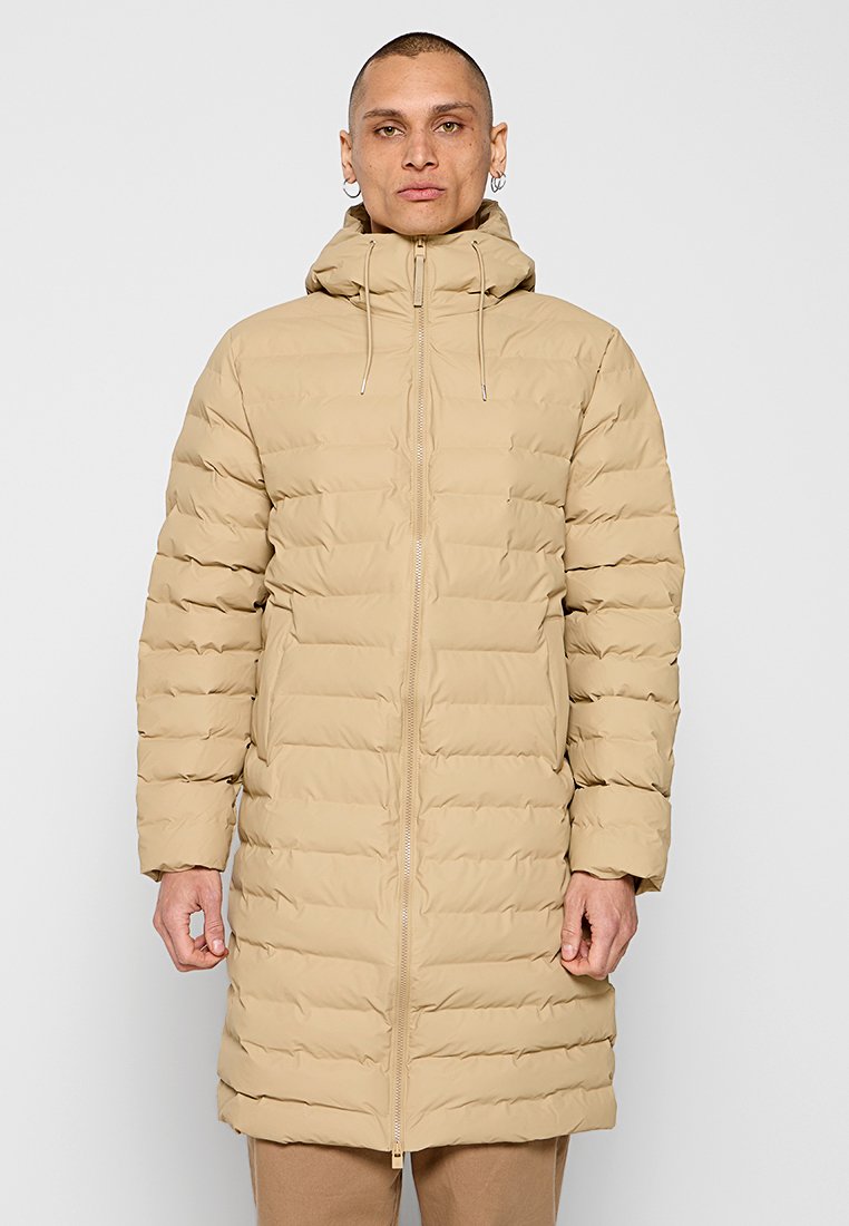 Beige gewatteerde lange jas met een rits aan de voorkant, een aanrandbare capuchon en horizontale stiksels. Heeft een relaxte pasvorm en is gemaakt van een gladde, lichte stof.