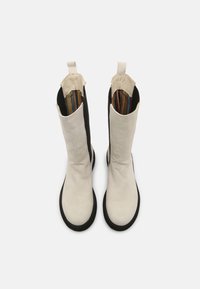 Białe skórzane botki za kostkę z czarnymi bokami, płaską podeszwą i podszewką z paskowanej tkaniny. Posiadają uchwyty na górze ułatwiające zakładanie.