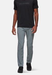 Szare spodnie outdoorowe wykonane z lekkiego materiału, o slim fit i kieszeniach cargo. W połączeniu z czarną koszulą z krótkim rękawem.