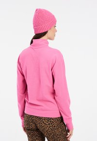 Vaaleanpunainen ribbipintainen fleece-pusero, jossa on kaulusta muistuttava kaulus, yhdistettynä ruskeisiin leopardikuvioisiin housuihin ja rakennepintaisiin vaaleanpunaisiin neulottuihin myssyyn.
