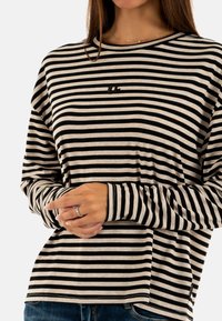 Gestreepte longsleeve shirt in zwart en crème, met een ronde halslijn, een relaxte pasvorm en een klein logo op de borst. Zacht, lichtgewicht stof.