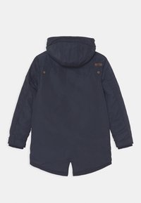 Námořnická modrá zateplená parka s kapucí, vybavená dvoucestným zipem, žebrovanými manžetami a čtvercovou nášivkou na horní části zad.