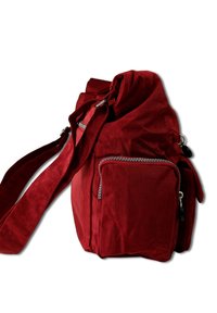 Rote Canvas-Umhängetasche mit weicher Textur, ausgestattet mit einer Klappenverschluss, verstellbarem Schulterriemen und einer kleinen Reißverschlusstasche auf der Vorderseite.