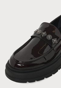 Mocassin bordeaux foncé brillant avec semelle noire épaisse et cinq clous décoratifs argentés sur la bride supérieure.