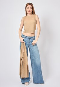 Crop top lavorato a maglia beige con un motivo a diamante testurizzato, abbinato a jeans a gamba larga blu chiaro. Un cardigan beige coordinato è appoggiato su un braccio.