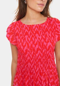 Robe texturée rouge et rose à manches courtes, présentant un design froncé et des motifs abstraits sur l'ensemble du tissu.
