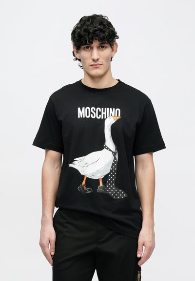 Čierne tričko s grafikou husy, ktorá má na sebe kravatu s bodkami a topánky, nad ňou je nápis „MOSCHINO“ v tučnom bielom písme.