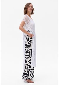 Witte gehaakte tuniek met korte mouwen, gecombineerd met hoog-waist zwart-wit gestreepte broek. Open zijkanten en een lichtgewicht textuur.