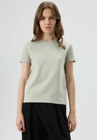 Lichtgroen T-shirt met korte mouwen, een ronde hals en een subtiele textuur. Gecombineerd met zwarte, wijde broek.