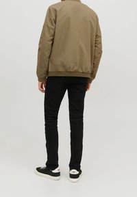 Bomber jacketki tummanvihreä, jossa on ribbireunukset ja hihansuut, yhdistettynä slim-fitteihin mustiin farkkuihin ja mustiin lenkkareihin, joissa on valkoiset pohjat.