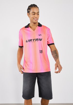 Pink gradient polo shirt with a black collar, featuring the logo "URTRN SPORTS" in black and the number "69" on the front. Black shorts.