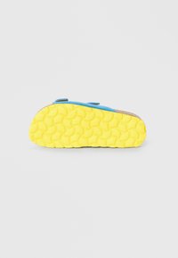 Μπλε υποδήματα με υφή κίτρινης σόλας που διαθέτει κυκλικά σχέδια. Περιλαμβάνει δύο λουριά με βέλκρο για κλείσιμο.
