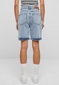 Shorts en jean bleu clair avec un ourlet effiloché, un design à cinq poches et une étiquette en cuir à la taille. La vue de dos montre une coupe décontractée.