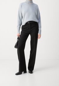  Lichtblauwe gebreide coltrui, relaxte pasvorm, met geribbelde boorden. Zwarte high-waisted broek, op maat gesneden, gecombineerd met zwarte hakken.