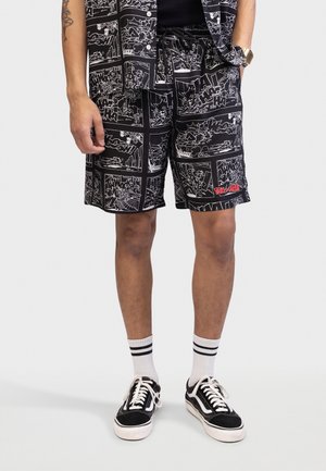 Svarte shorts med tegneseriestrekninger i hvitt, med "Tom & Jerry"-logo i rødt. Kombinert med hvite stripete sokker og svarte joggesko.
