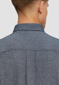 Denim shirt met een gestructureerde kraag en schouderdetail. De stof is textuurgegeven met een blauw visgraatpatroon. Subtiele stikaccenten.