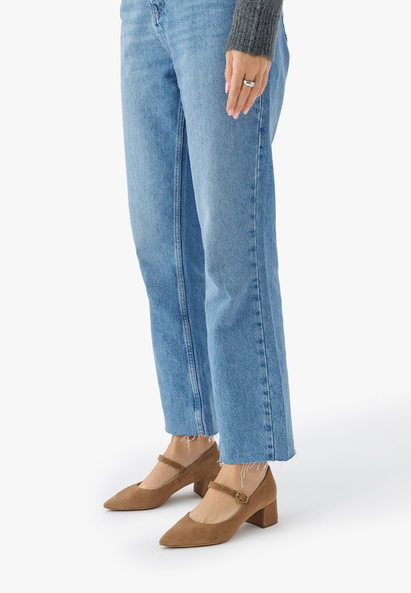 Pantofi din Suede maro cu toc bloc, cu vârful ascuțit și curea la gleznă, asortați cu blugi din denim de un albastru deschis cu margini destramate.