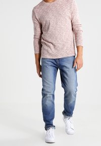 Lätt texturerad, rosenfärgad långärmad skjorta, kombinerad med klassiska blå jeans och vita sneakers, som visar en avslappnad passform och en ledig stil.