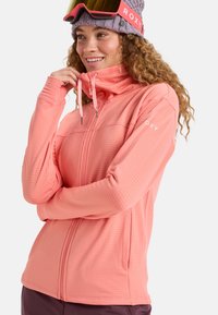Roxy pink zip-up jacket with ribbed texture, side pockets, and adjustable hood. Model wearing a knit hat and ski goggles.