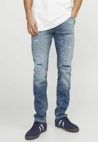 Vaqueros de mezclilla azul claro con un ajuste slim, detalles desgastados con desgarrones y un lavado desvanecido. Combinados con zapatillas oscuras.