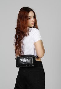 Bolso de mano de cuero negro con herrajes plateados, que presenta un diseño alado y un logo en relieve. Forma compacta y rectangular con acentos de tachuelas.