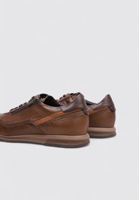 Zapatillas de cuero marrón con una textura suave, un diseño aerodinámico y acentos en contraste. Incluyen cordones y punta redondeada.