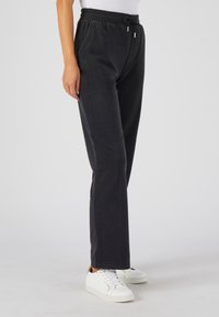 Zwarte fleece joggers met een elastische tailleband en trekkoord, voorzien van zijzakken en taps toelopende pijpen, gecombineerd met witte sneakers.