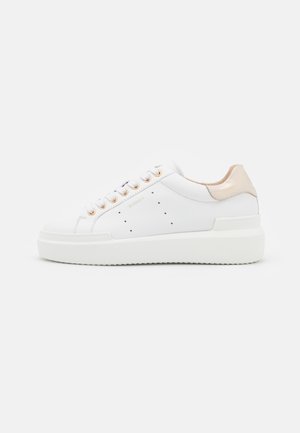 Hvid lavtopet sneaker med tyk sål, guldøjer, perforerede sidedetaljer og lys beige hælaccents.