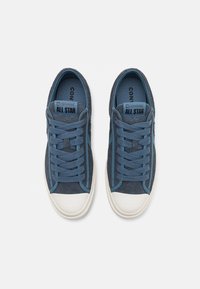 Ténis de camurça azul com detalhes em azul claro, bico redondo, sola de borracha branca e cordões planos. Marcação "Converse All Star" na língua.