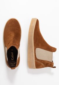 Scarpe slip-on in suede marrone con pannelli elastici laterali, accenti beige testurizzati e una suola in gomma testurizzata. Dettagli di cucitura sottili visibili.