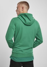 Zelená mikina s kapucí a přední kapsou, se stahovací šňůrkou, žebrovanými manžetami a dolním lemem. Měkká tkanina s hladkým povrchem, minimalistický design.