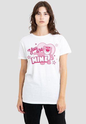 Young woman wearing white t-shirt with pink cartoon bear, heart, stars, and text "You are Mine" on a light gray background.