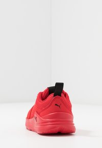 Chaussure de sport rouge avec tige en maille et accents noirs. Elle présente un talon texturé et une languette arrière pour un enfilage facile. Semelle en caoutchouc pour une meilleure adhérence.