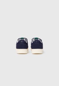 Pantofi din suede navy, cu un design low-top, talpă din cauciuc albă și accente verzi pe tab-ul călcâiului. Caracteristici include cusături minime și detalii cu logo.